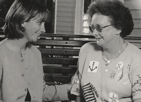 Black and white photo of Holly Benson and her grandmother, Louise, sitting side by side on a bench and smiling at each other